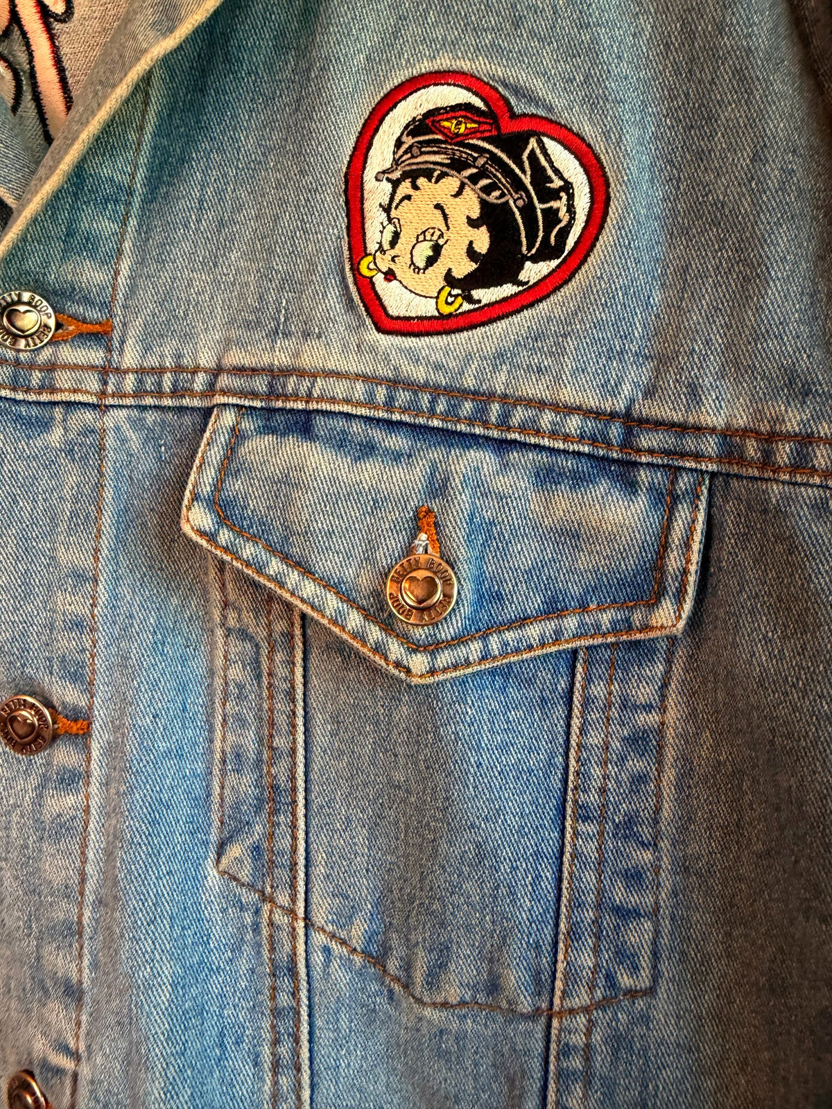 225 Threadz light-wash denim jacket featuring a Betty Boop heart patch and custom branded metal buttons.