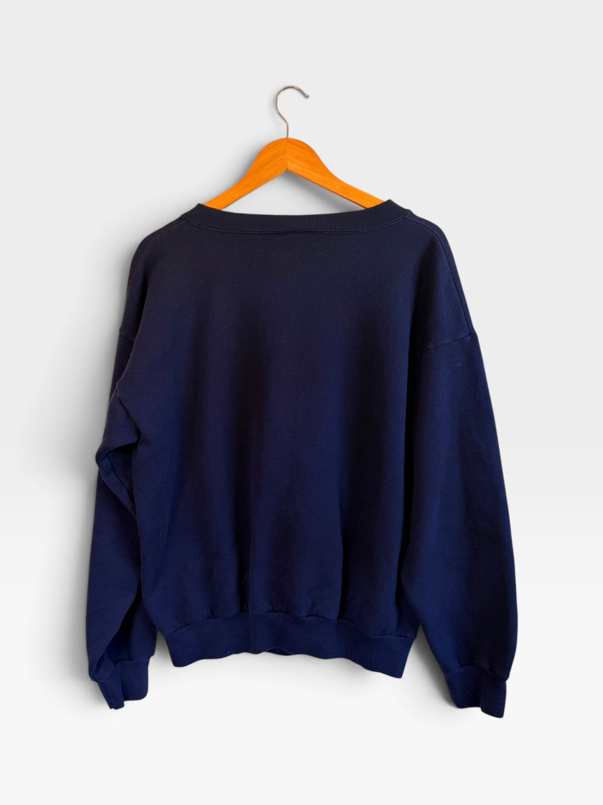 Back view of a 225 Threadz navy blue crewneck sweatshirt hanging on a wooden hanger against a plain white wall.