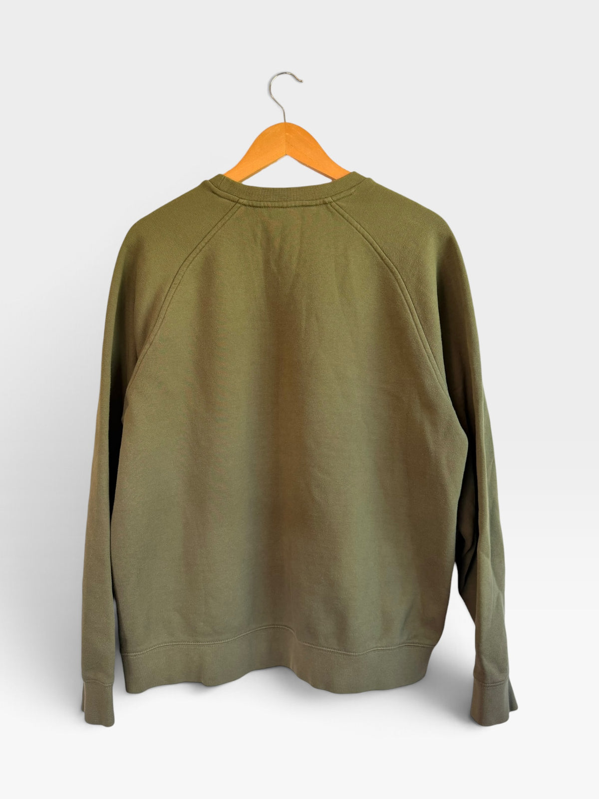 225 Threadz olive green Nike crewneck sweatshirt with raglan sleeves hanging on a wooden hanger against a white wall.